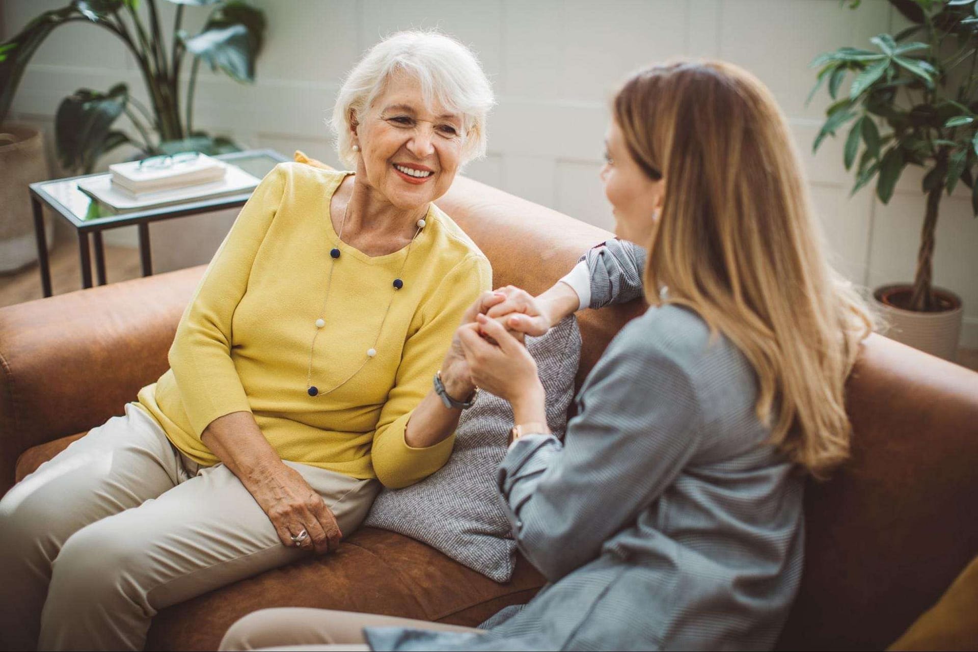 Family Conversation About Senior Living - The Preserve A woman sits on a couch and holds hands with a family member to discuss senior living options.